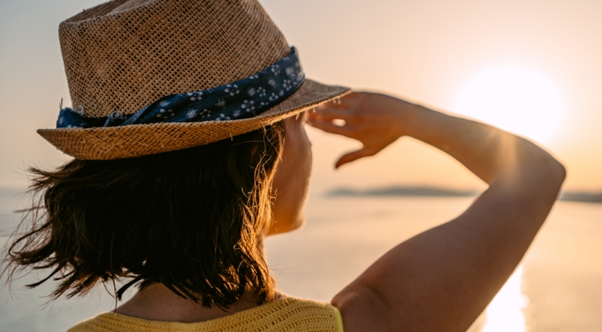 woman in a hat staring out at sunset while shading her eyes with her right hand